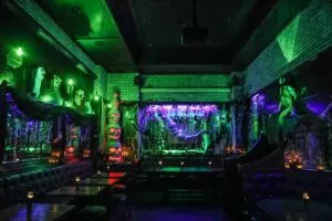 Fotografía editorial de un cóctel púrpura servido en una copa ahumada, con calabazas iluminadas, velas y decoración de Halloween en un bar neoyorquino.
